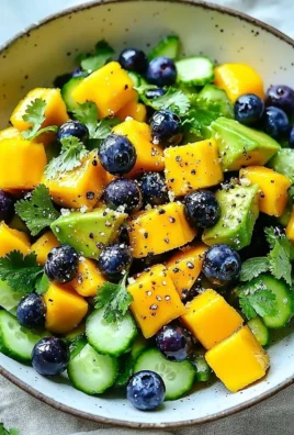 Juicy mango cucumber salad topped with blueberries and avocado for a fresh summer dish.