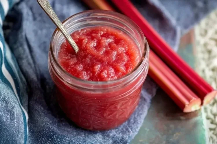 Delicious homemade rhubarb sauce in a glass jar with fresh rhubarb stalks