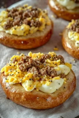 Sausage, egg, and cheese breakfast bagels stacked on a plate.