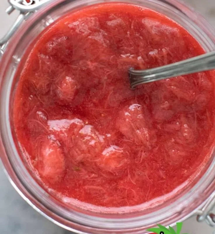 Homemade strawberry rhubarb sauce in a glass jar with fresh strawberries and rhubarb.