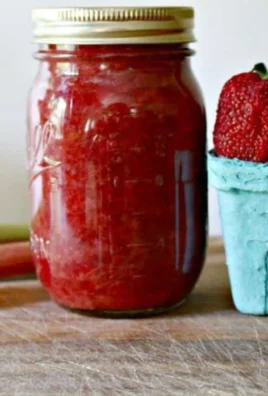 Homemade strawberry rhubarb sauce in a bowl with fresh strawberries and rhubarb stalks.