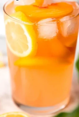 Refreshing glass of peach lemonade garnished with fresh peaches and mint