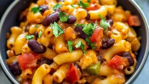 A steaming bowl of delicious vegetarian chili mac topped with fresh herbs.