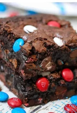 Plate of fudgy ultimate gooey brownies topped with chocolate drizzle and nuts