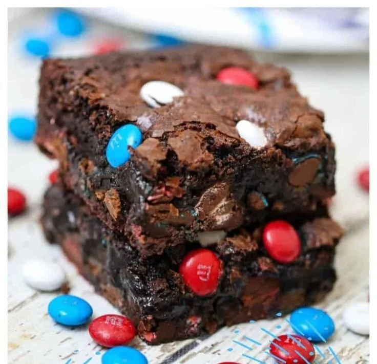 Plate of fudgy ultimate gooey brownies topped with chocolate drizzle and nuts