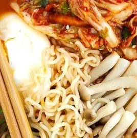 Bowl of spicy kimchi ramen topped with vegetables and a soft-boiled egg.