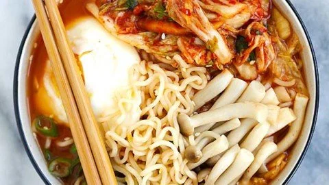 Bowl of spicy kimchi ramen topped with vegetables and a soft-boiled egg.