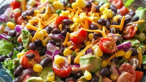 A vibrant cowboy salad with fresh vegetables, beans, and dressing in a bowl.