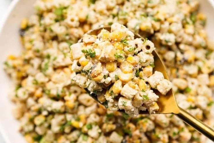 Creamy elote pasta salad with corn and zesty dressing in a bowl.