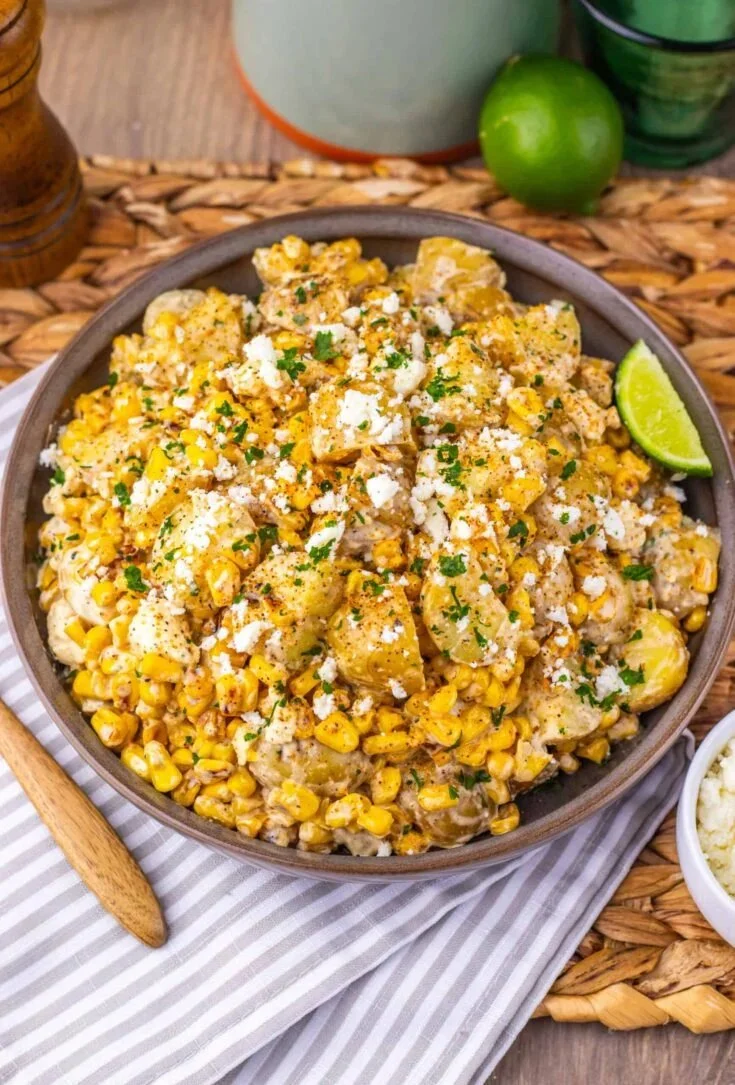 Loaded Mexican street corn potato salad in a bowl, garnished with cilantro and lime